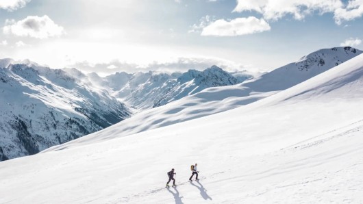 Sneeuwfoto van een besneeuwde berghelling met twee wandelaars