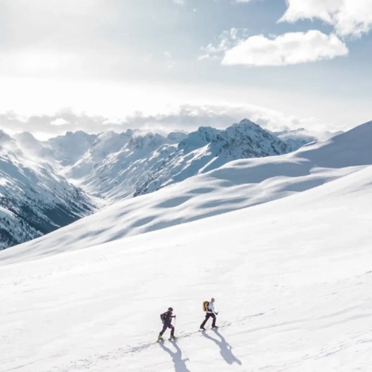 Sneeuwfoto van een besneeuwde berghelling met twee wandelaars